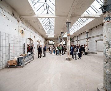 Teilnehmende des Runden Tisch Darstellende Kunst stehen in einem leeren großen Raum des Hauses der Produktion