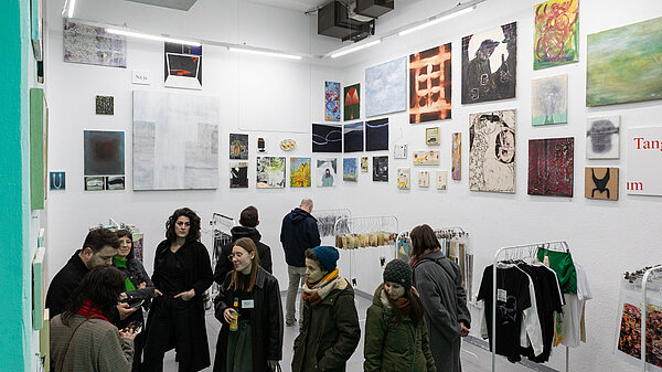 Personen in einem weißen hohen Raum mit sehr vielen Kunstwerken bis unter die Decke