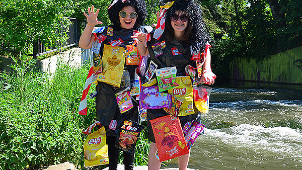 Zwei Schülerinnen, die auf einem Stein vor einem Fluss stehen und als Monster mit Perrücke und Mülltüten verkleidet sind.