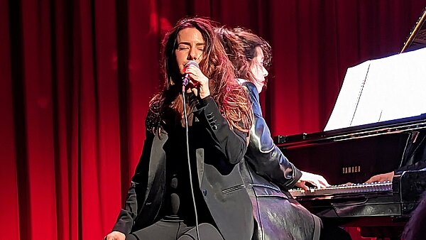 Eine Sängerin, Rücken an Rücken mit einer Pianistin auf einer Bühne